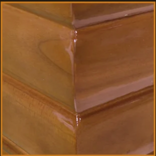 Zoom sur l’angle d’un cercueil en bois vernis, finition lisse et chaleureuse – essence naturelle haut de gamme